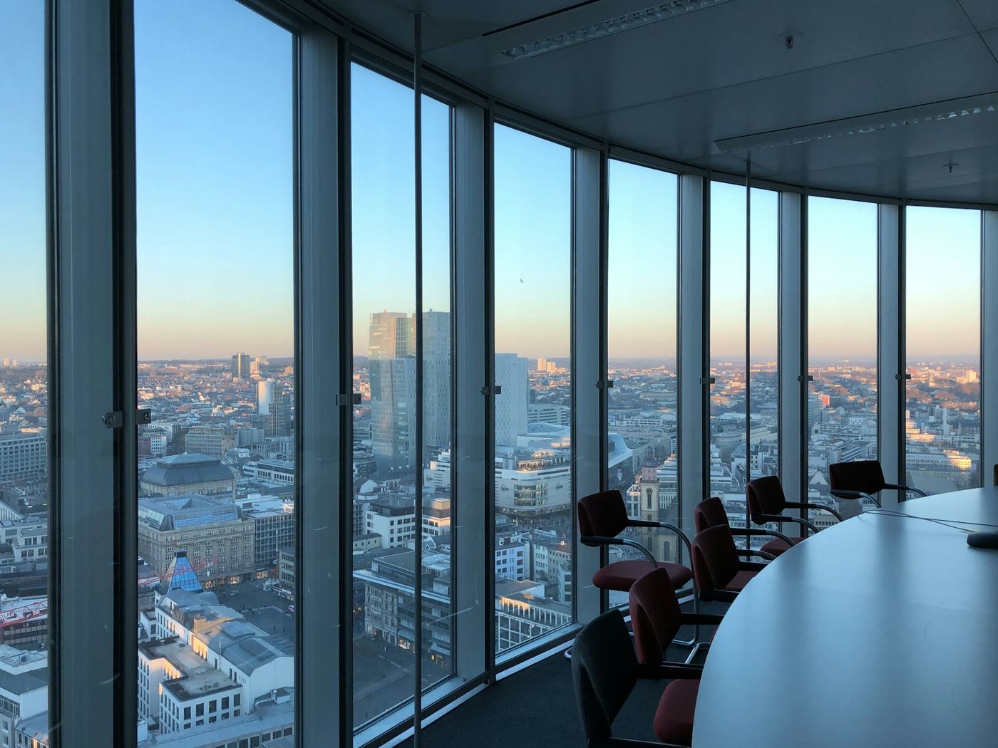 A curved glass wall in a high-rise office looking out over a city at sunset